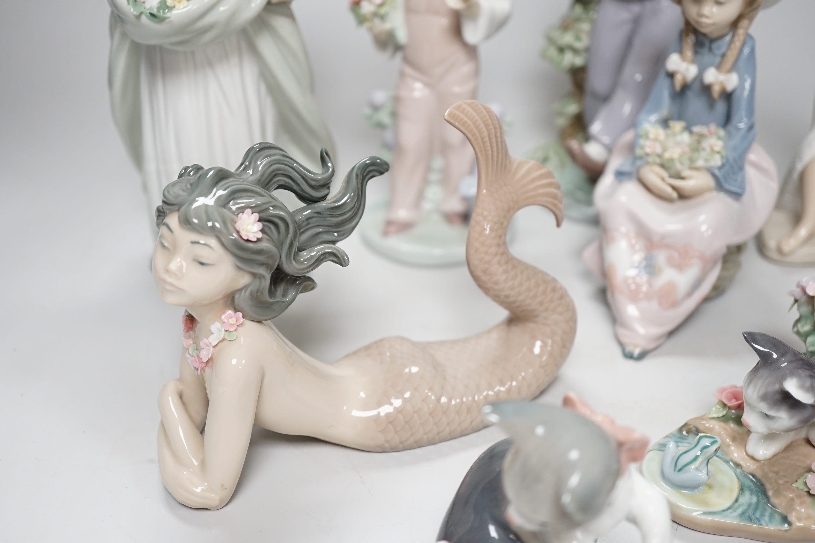 A large Lladro figure of a flower girl, mermaid, boy playing a drum and five other models including a Nao example, the largest 24cm high (8)